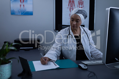 Matured female doctor writing on medical file in clinic