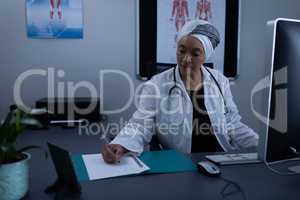 Matured female doctor writing on medical file in clinic