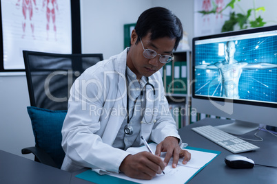 Confident male doctor writing on medical file in clinic