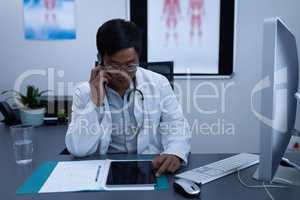 Doctor talking on mobile phone while using digital tablet