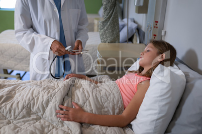 Matured female doctor examining girl on bed in clinic