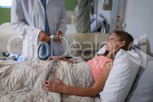 Matured female doctor examining girl on bed in clinic