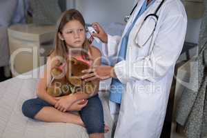 Matured female doctor using otoscope for checking girl ear