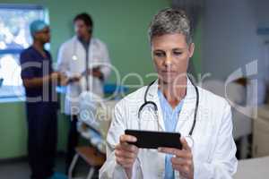 Matured female doctor using mobile phone in clinic at hospital