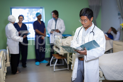 Confident male doctor looking medical report in clinic at hospital