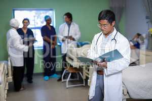 Confident male doctor looking medical report in clinic at hospital