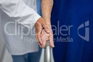 Doctor holding hand of senior patient while walking with walker in hospital clinic