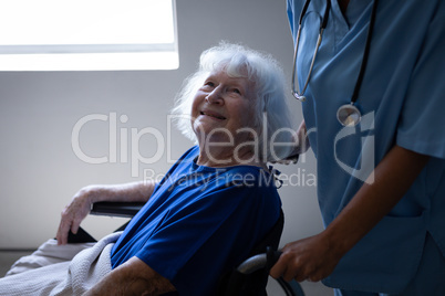Female surgeon pushing the wheelchair of a disabled senior patient at hospital corridor