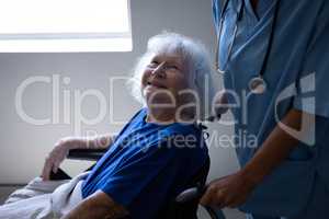 Female surgeon pushing the wheelchair of a disabled senior patient at hospital corridor