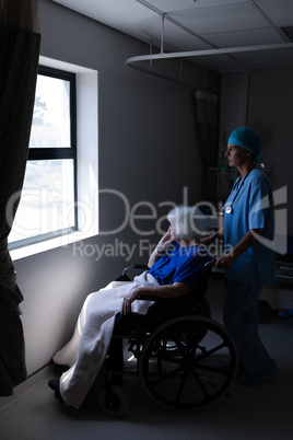 Female surgeon holding wheelchair while senior patient looking outside the window