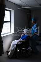 Female surgeon holding wheelchair while senior patient looking outside the window