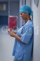 Female surgeon using mobile phone in hospital corridor