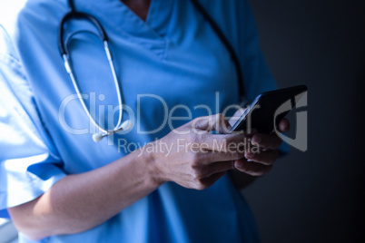 Female surgeon using mobile phone in hospital corridor