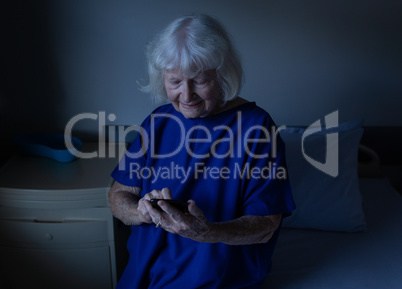 Senior female patient using a mobile phone at hospital bed