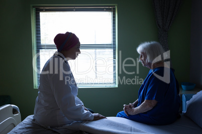 Mature female doctor talking with senior patient in hospital room