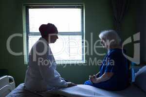 Mature female doctor talking with senior patient in hospital room