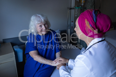 Mature female doctor talking with senior patient in hospital room