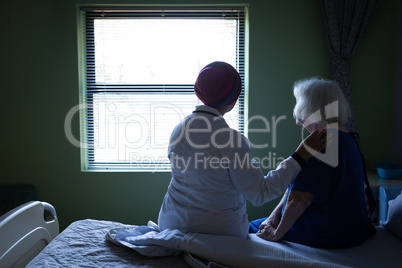 Female doctor and senior woman looking outside through the window