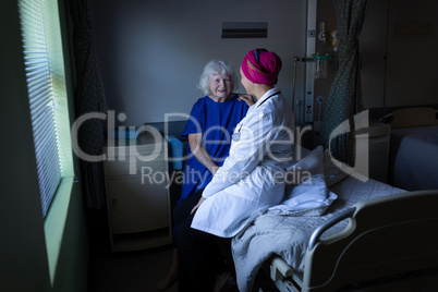 Mature female doctor talking with a senior patient in hospital room