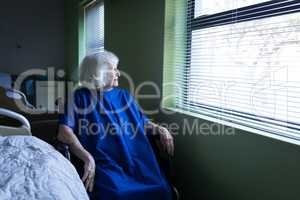 Senior female patient looking outside through the window at hospital room