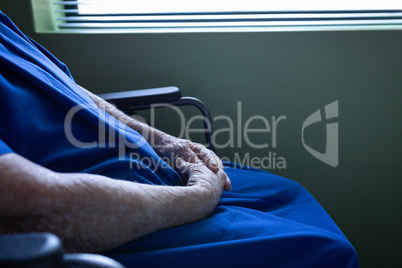 Senior female patient sitting on wheelchair with hand clasped