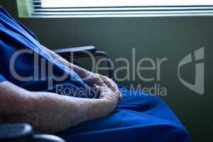 Senior female patient sitting on wheelchair with hand clasped