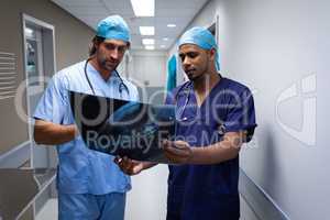 Male surgeons discussing over x-ray report at hospital corridor