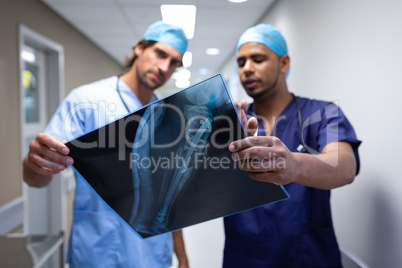 Male surgeons discussing over x-ray report at hospital corridor