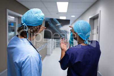 Male surgeons discussing over x-ray report at hospital corridor