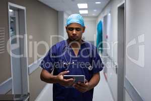 Male surgeon using digital tablet while standing at hospital corridor
