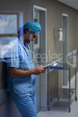 Male surgeon using mobile phone at hospital corridor