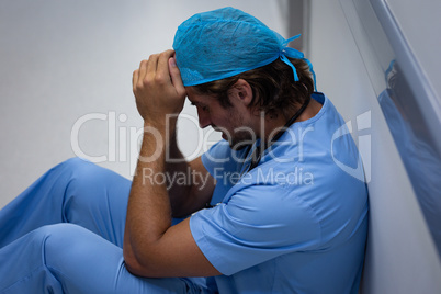 Depressed male surgeon sitting and leaning in the corridor at hospital