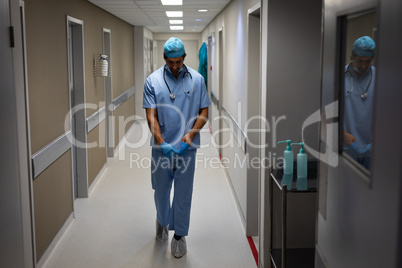 Male surgeon removing rubber gloves while walking at hospital corridor