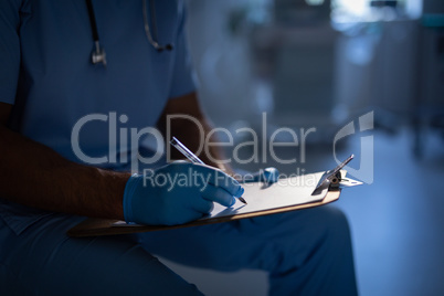 Male surgeon writing a report on paper at hospital