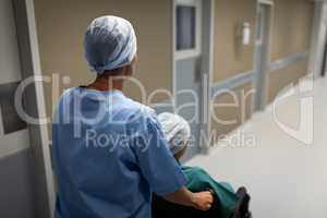 Female surgeon pushing patient wheelchair at hospital corridor