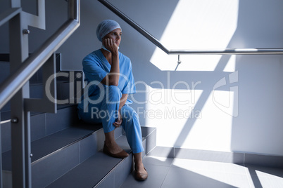 Female surgeon sitting on stair case in hospital