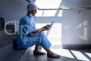 Female surgeon using mobile phone while sitting on hospital stair case