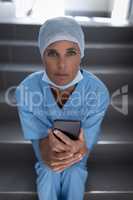 Female surgeon sitting on stair case while holding mobile phone