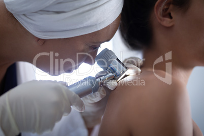 Female doctor checking woman body with dermatoscopy