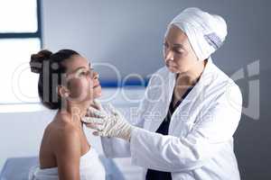 Mature female doctor checking neck of woman in clinic