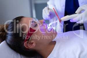 Female dentist examining patient with dental curing light in clinic