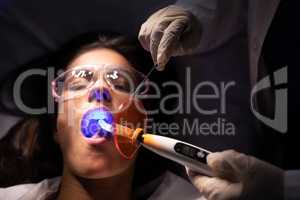 Dentist examining patient with dental curing light in clinic