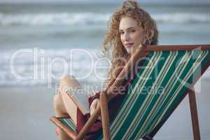 Woman holding book while sitting on sun lounger at beach