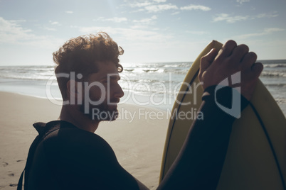 Male surfer with a surfboard standing on a beach