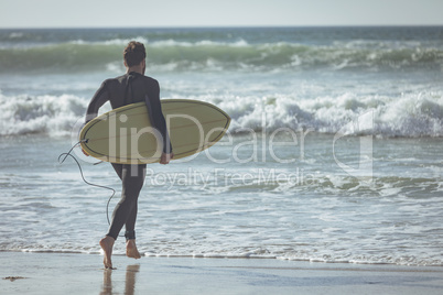 Male surfer with a surfboard running on a beach
