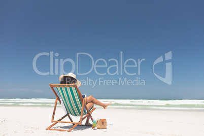 Young woman using digital tablet while sitting at sun lounger at beach