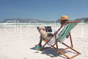 Young man using laptop while sitting at sun lounger at beach