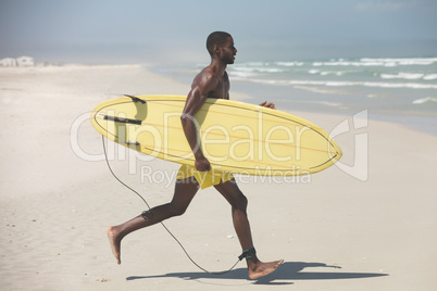 Male surfer with a surfboard running on a beach on a sunny day
