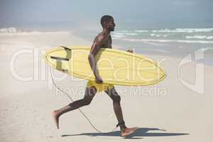 Male surfer with a surfboard running on a beach on a sunny day