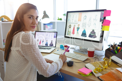 Female fashion designer looking at camera while working at desk